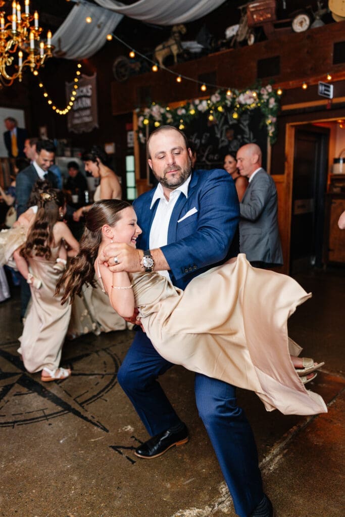 Father and daughter dancing at rustic wedding reception.