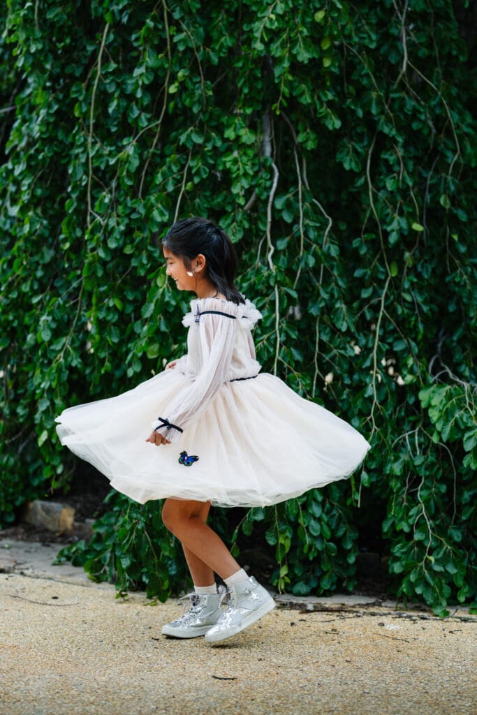Young girl twirling in a white dress beneath cascading greenery at Grounds For Sculpture in Hamilton Township, New Jersey.
