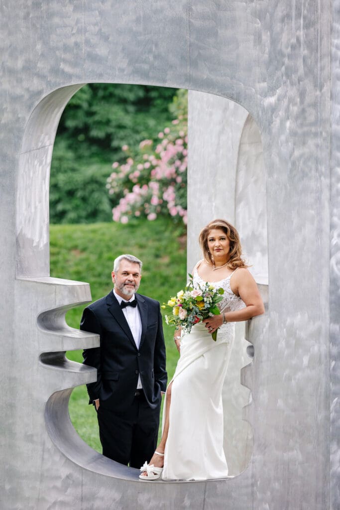 Couple posing within a sculpture at Grounds For Sculpture during their 25th wedding anniversary vow renewal in New Jersey.
