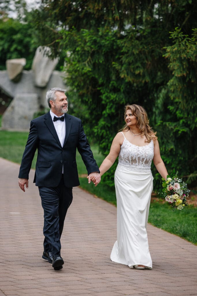 Couple walking hand in hand through Grounds For Sculpture during a 25th wedding anniversary celebration in Hamilton Township, NJ.