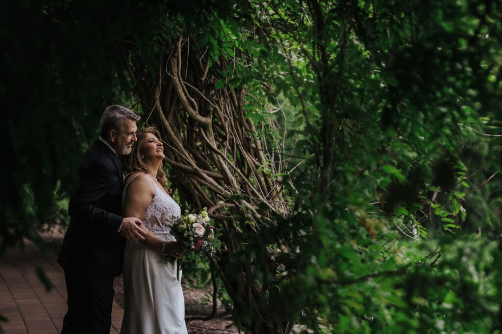 Romantic portrait of a couple surrounded by lush greenery during their 25th wedding anniversary vow renewal at Grounds For Sculpture.